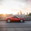 Red Italian Alfa Romeo sportscar driving across a bridge, a city skyline visible in the background.