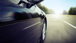 Closeup of the door of a speeding car on a highway, trees visible in the background