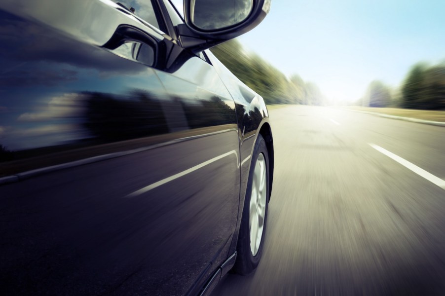 Closeup of the door of a speeding car on a highway, trees visible in the background