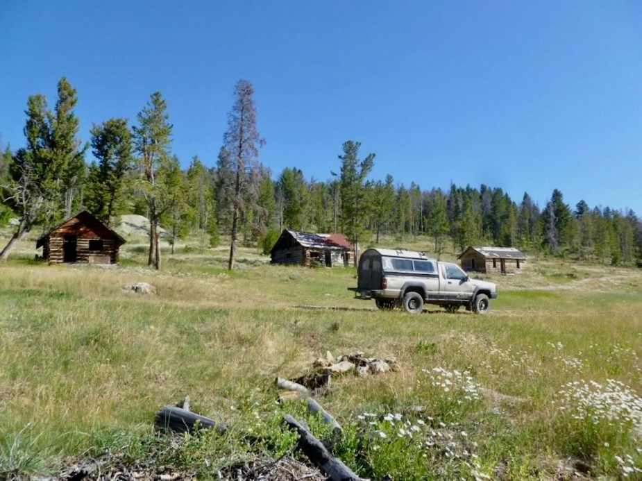 A truck parked by cabins in a ghost town in the state of Montana.