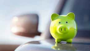 A green piggy bank sits atop a silver car's hood in close right front view