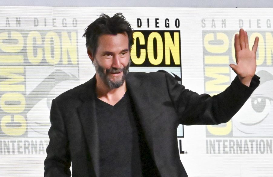 Keanu Reeves dressed in black waving in front of 2024 San Diego International Comic-Con banner in July 2024