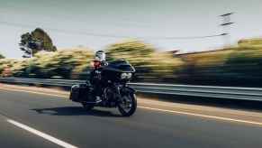 Man riding a motorcycle fast on US road in right front and side angle view with power lines and trees blurred in background