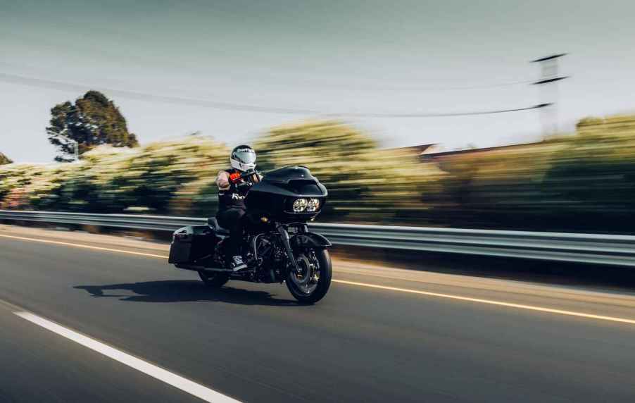 Man riding a motorcycle fast on US road in right front and side angle view with power lines and trees blurred in background