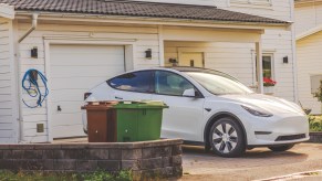 A white Tesla EV parked outside a home garage on the driveway