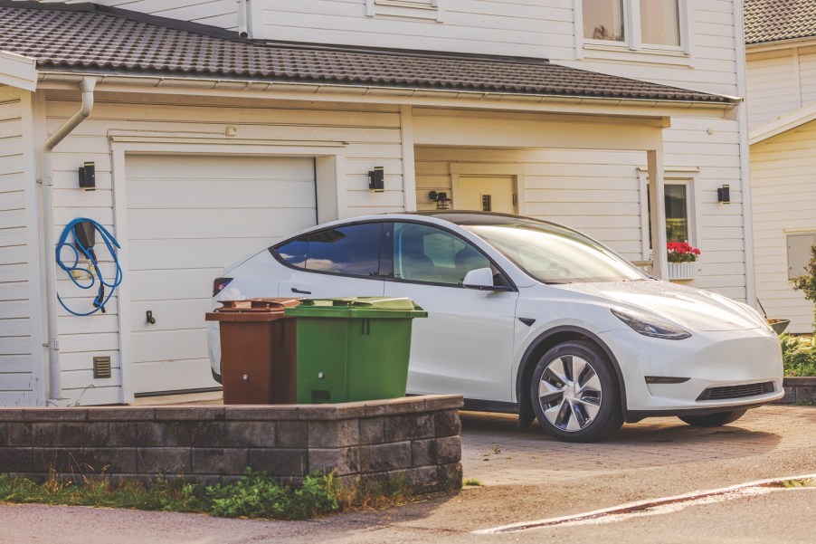 A white Tesla EV parked outside a home garage on the driveway