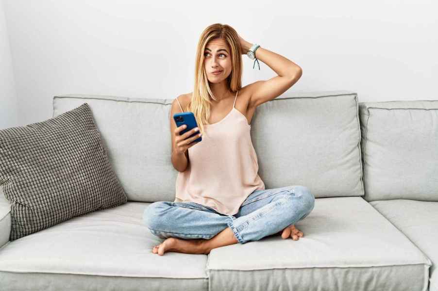 A woman sits on couch with cell phone confused expression depicting not understanding Instagram captions