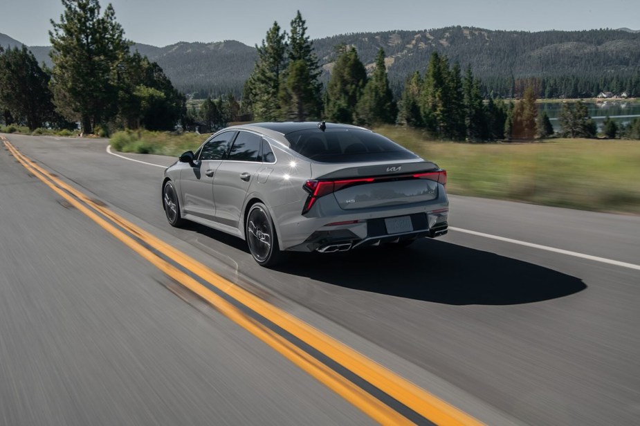 Gray Kia K5 sports sedan driving away on a country road.