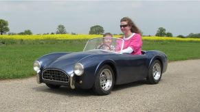 A family enjoys a mini dream car representation with a tiny Shelby Cobra from Harrington Junior Cars.