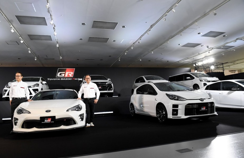 Akio Toyoda, company VP stands between two white Toyota sports cars in the Gazoo Racing show room.