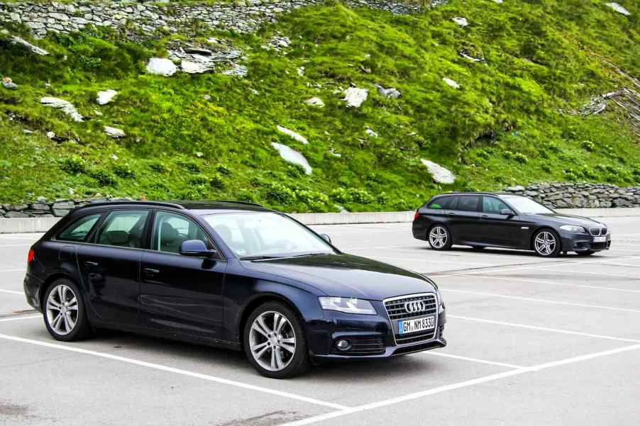 Two black station wagon cars on an alpine road in Austria, a mountainside visible in the background.