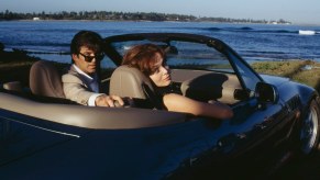 James Bond and his passenger look backward out of a BMW Z3 convertible during the "Goldeneye" film, the ocean visible in the background.