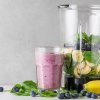 A pile of fruit and a smoothie around a blender on a kitchen countertop.