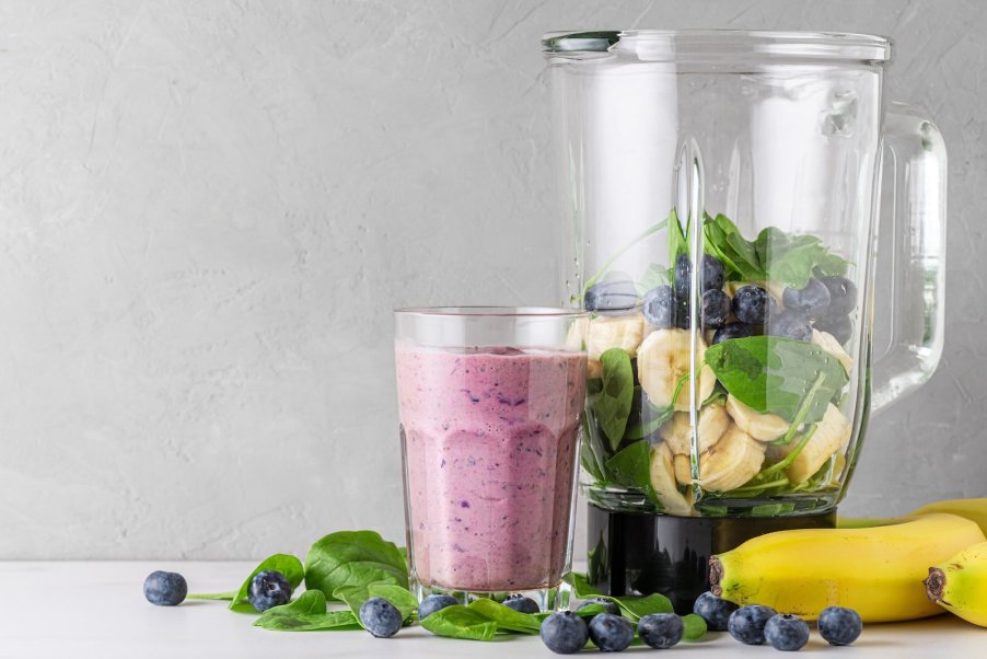 A pile of fruit and a smoothie around a blender on a kitchen countertop.