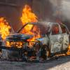 Car parked on a city street and engulfed in flames.