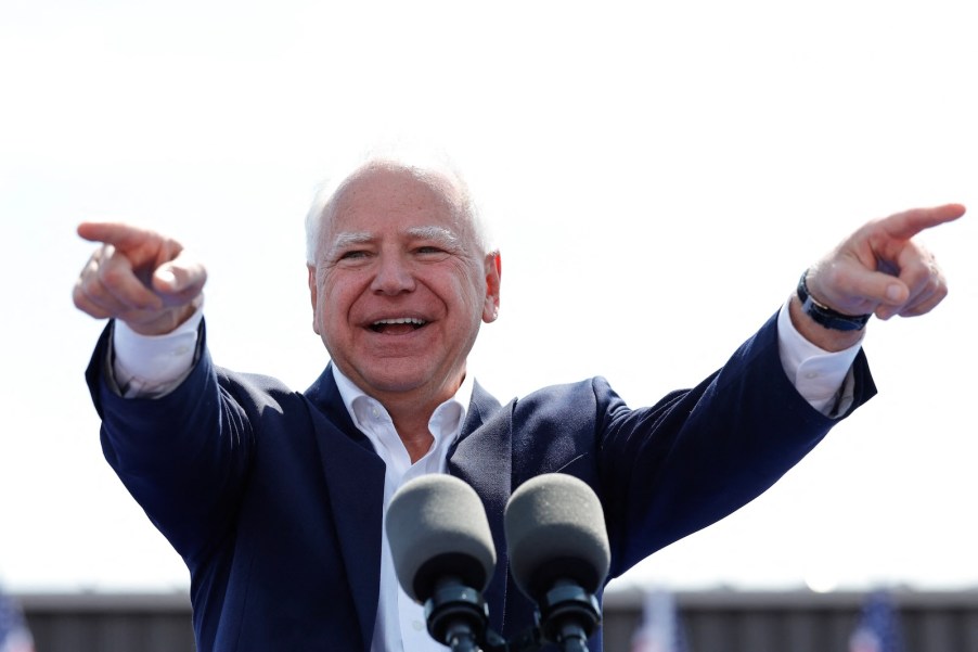 Tim Walz stands at a podium during a speech and points at the audience.