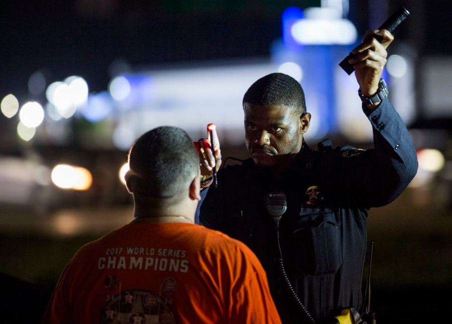 Police officer holds a flashlight and pen in front of a driver during a nighttime field sobriety test.