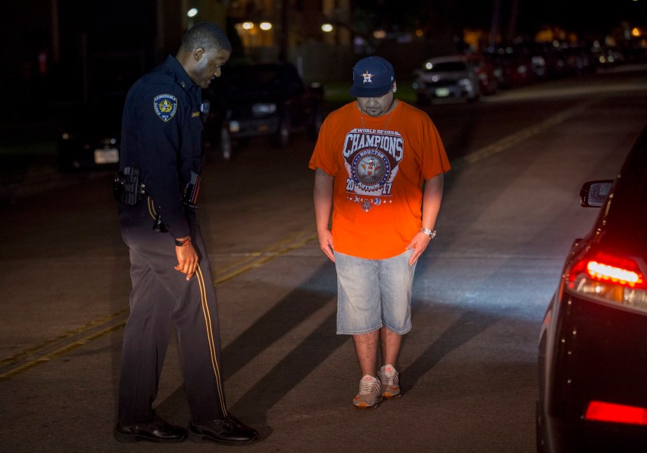 Police officer standing next to a man on a nighttime street, directing him through a field sobriety test