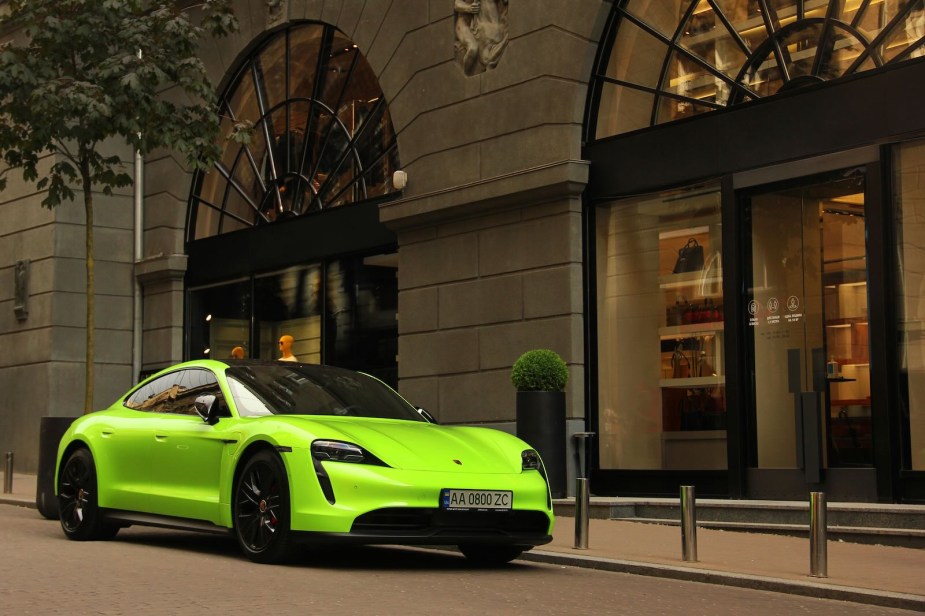 Lime green Porsche Taycan Turbo S sedan parked in front of a fancy hotel, people walking by on the street.