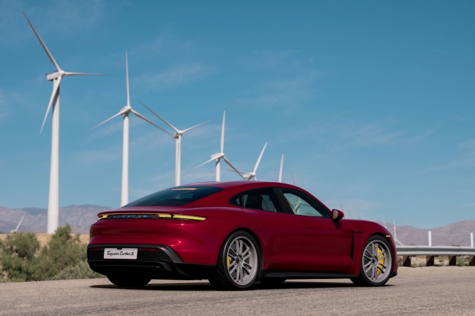 Red Porsche Taycan supercar in front of a row of windmills.