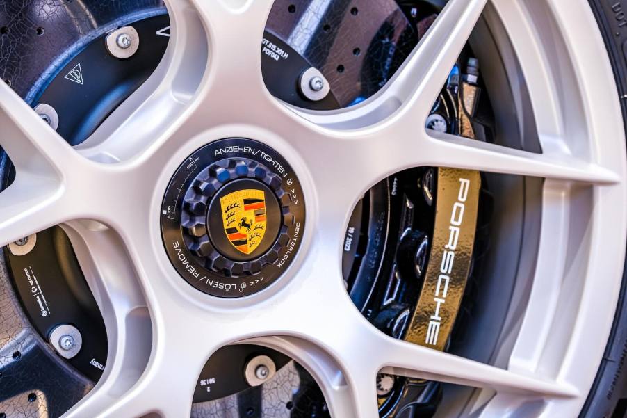 The Porsche crest logo in the center lug of a supercar rim, its brake calipers visible in the background