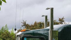 The upward-facing exhaust stacks above a semi truck tractor, trees visible in the background.