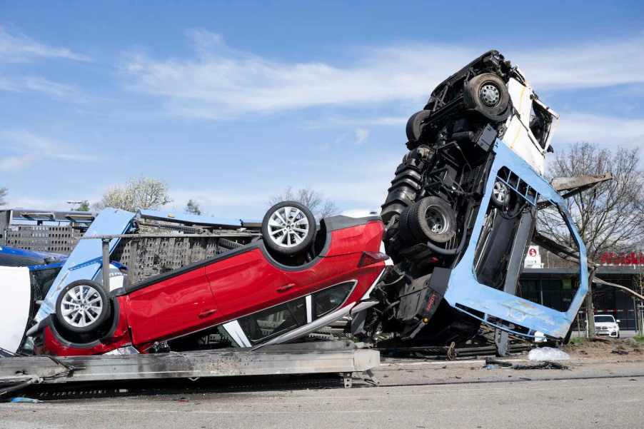 Overturned car transport truck on the highway, a crashed exotic car visible in the foreground.