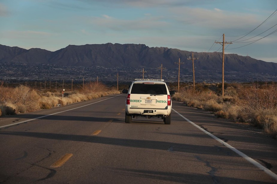 White U.S. border Patrol SUV driving down the highway, mountains visible in the background.