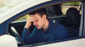 Frustrated male driver, possibly upset over negative equity on his car loan, holds head in one hand against steering wheel