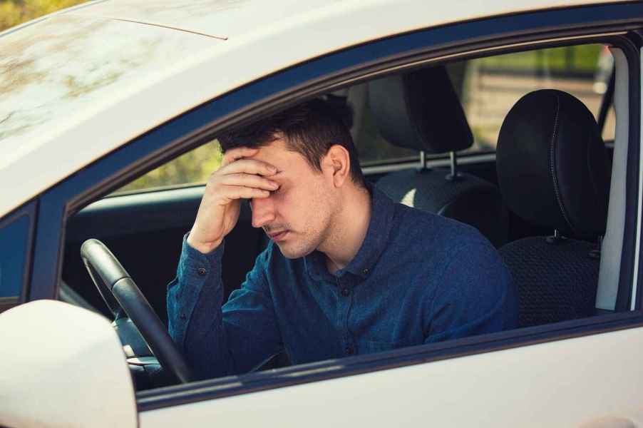 Frustrated male driver, possibly upset over negative equity on his car loan, holds head in one hand against steering wheel