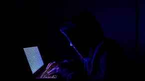 A person sitting at a laptop computer in the dark attempting to hack into a mainframe