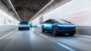 Two Tesla Cybertrucks driving over a covered road, looking as though they're driving fast