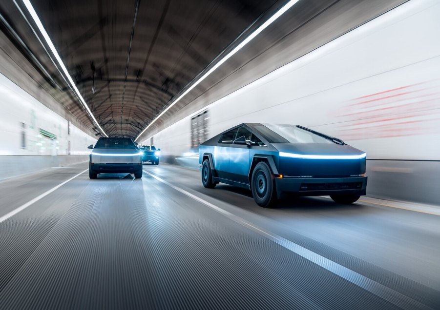 Two Tesla Cybertrucks driving over a covered road, looking as though they're driving fast