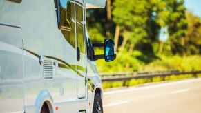 An RV driving in close right front side view with blurred sunny, treelined background