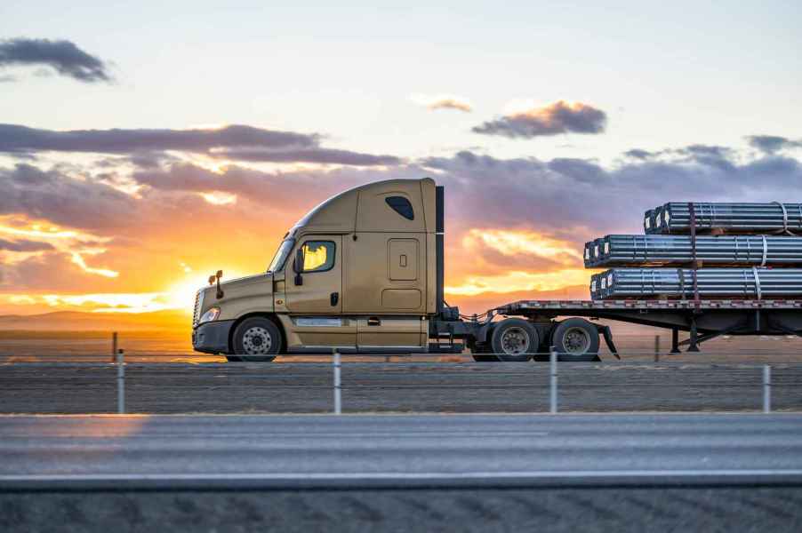 A semi-truck parked in left profile view with a steel rod load