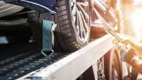 Tow truck driver hand secures vehicle on flatbed truck