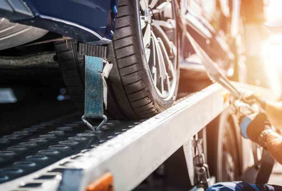 Tow truck driver hand secures vehicle on flatbed truck