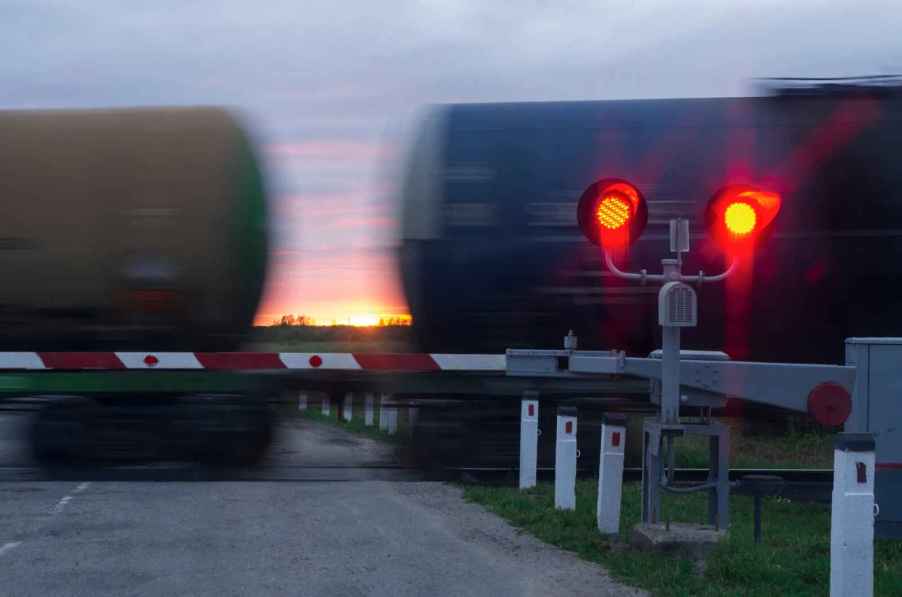 Train passing viewer at dusk with red crossing lights on