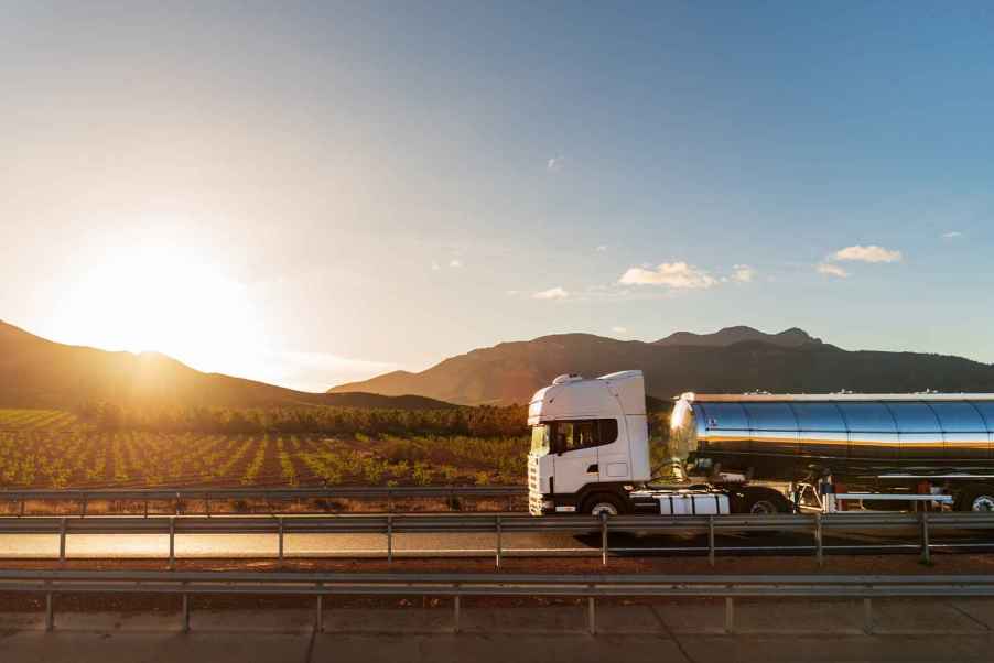 A tanker truck hauling wine drives down a road in front of a vineyard