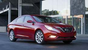 A red 2012 Hyundai Sonata parked in right angle view with headlights on