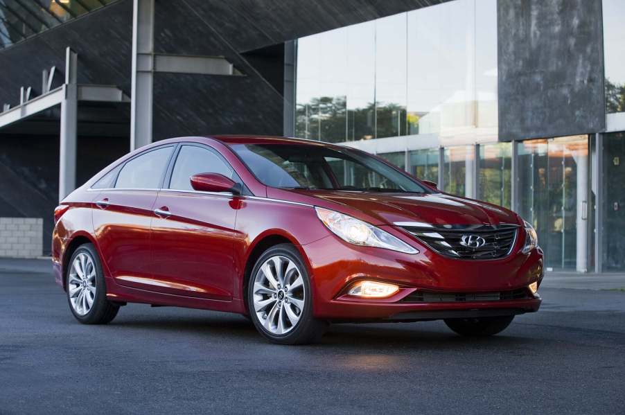 A red 2012 Hyundai Sonata parked in right angle view with headlights on