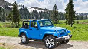 A blue 2012 Jeep Wrangler parked in a green forested area in right front angle view