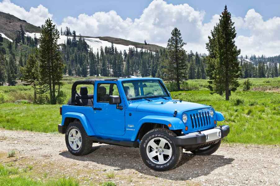 A blue 2012 Jeep Wrangler parked in a green forested area in right front angle view