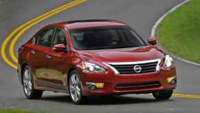 A dark red 2013 Nissan Altima driving on the road