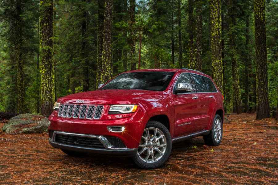 A red 2014 Jeep Grand Cherokee parked in a wooded area in right front angle view