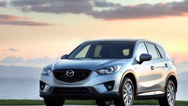 A silver 2014 Mazda CX-5 parked outside in left front angle view at dusk