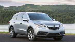 A silver 2015 Acura MDX parked in front of water and a mountain in right front angle view