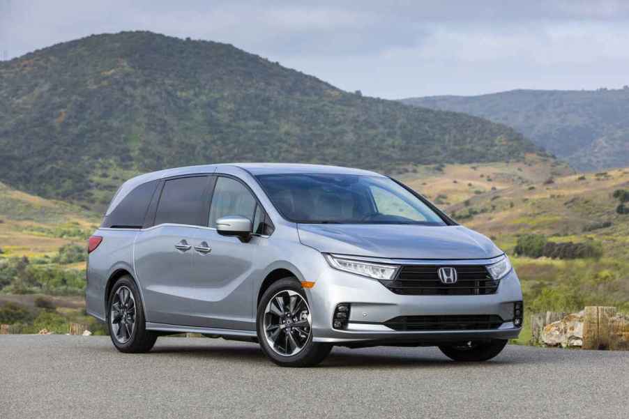 A silver 2021 Honda Odyssey parked in front of a green mountain range in right front angle view