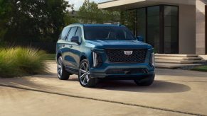 A metallic blue 2025 Cadillac Escalade-V parked in front of a modern home in right front angle view