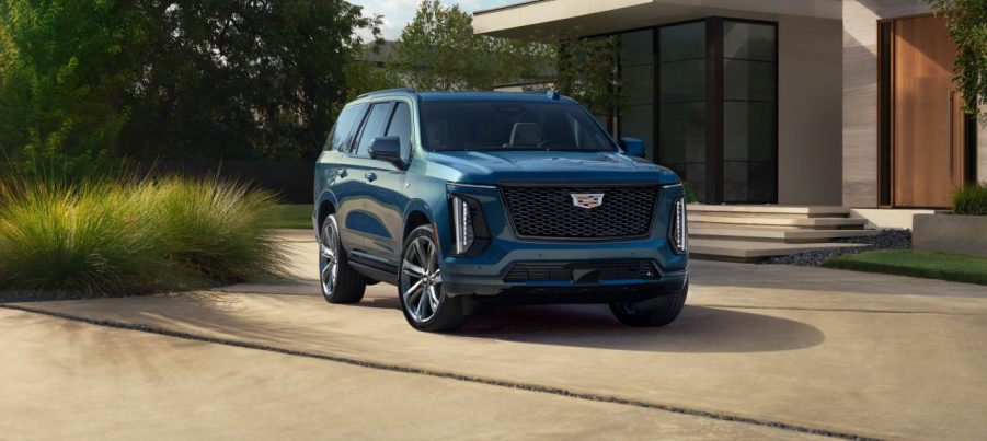 A metallic blue 2025 Cadillac Escalade-V parked in front of a modern home in right front angle view